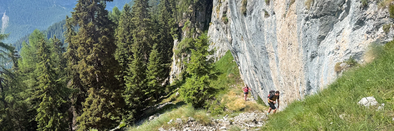 Two hikers walking along a cliffside trail from Lago di Tovel toward Monte Peller in the Brenta Dolomites