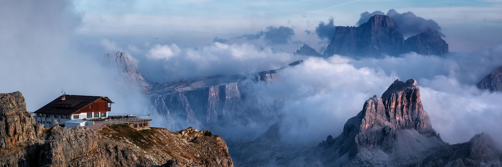 Rifugio Lagazuoi mountain hut facing the Nuvolau, Croda da Lago and Monte Pelmo ranges under a clear sky with valley clouds