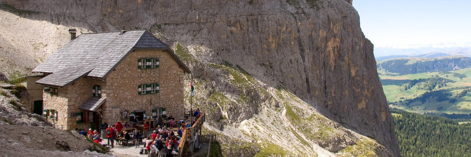 Busy midday terrace at Langkofelhutte mountain hut beneath the massive rock walls of Sasso Piatto in the Dolomites