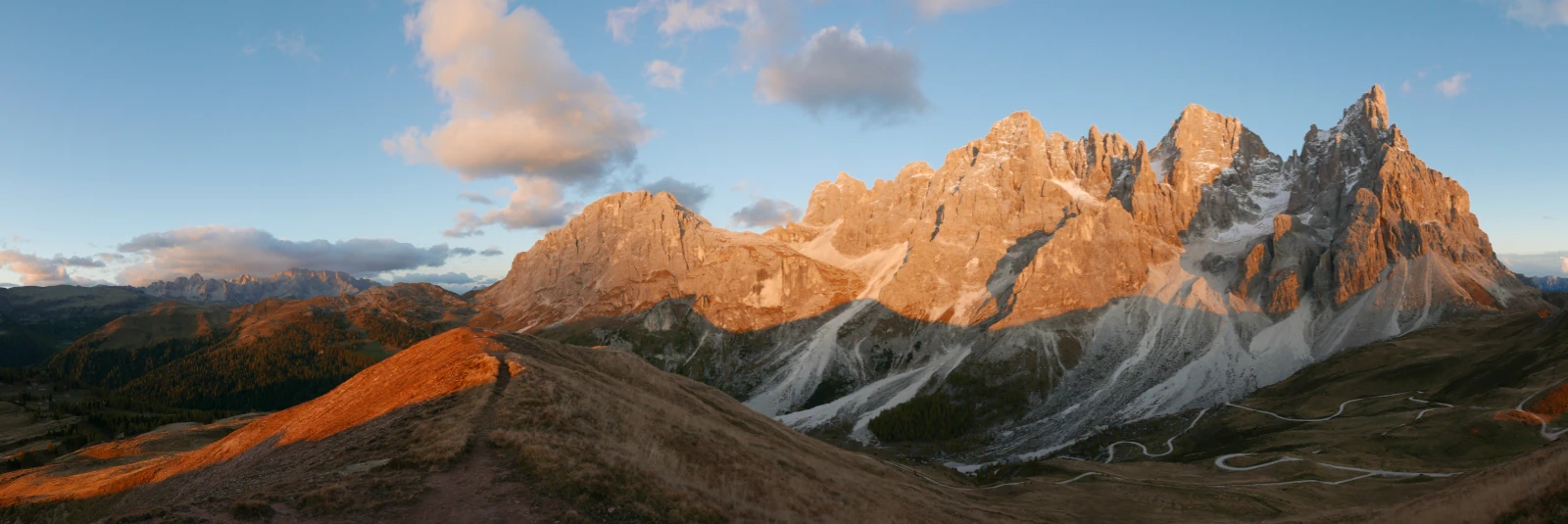 Autumn alpine trail at Passo Rolle facing the Cimon della Pala peak with the distant Civetta group at sunset